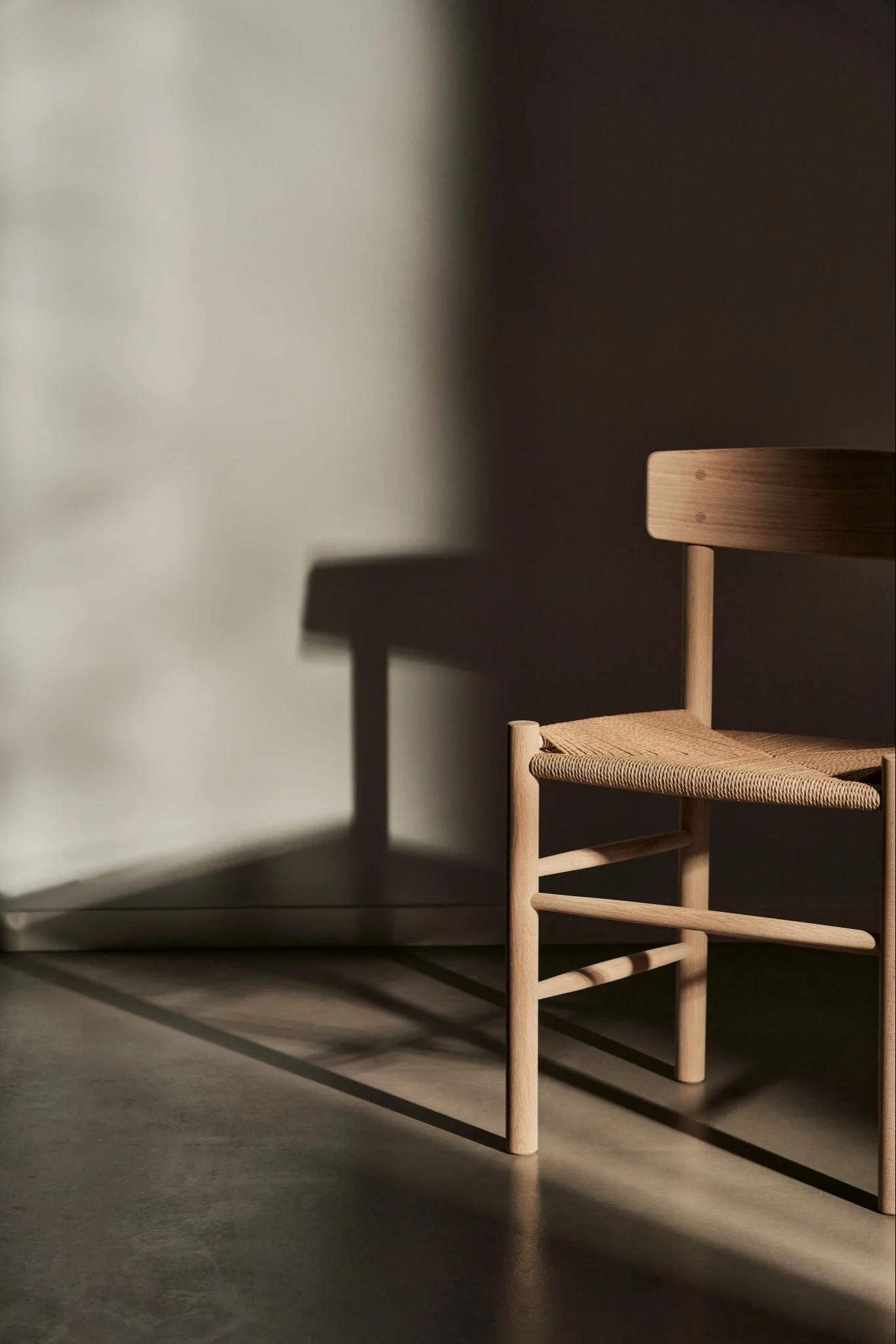 Wooden chair with woven seat in a room with strong shadows on the wall.