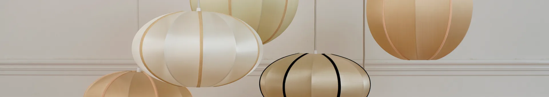 Close-up of several elegant hanging lamps with ribbed fabric shades in various light colors.