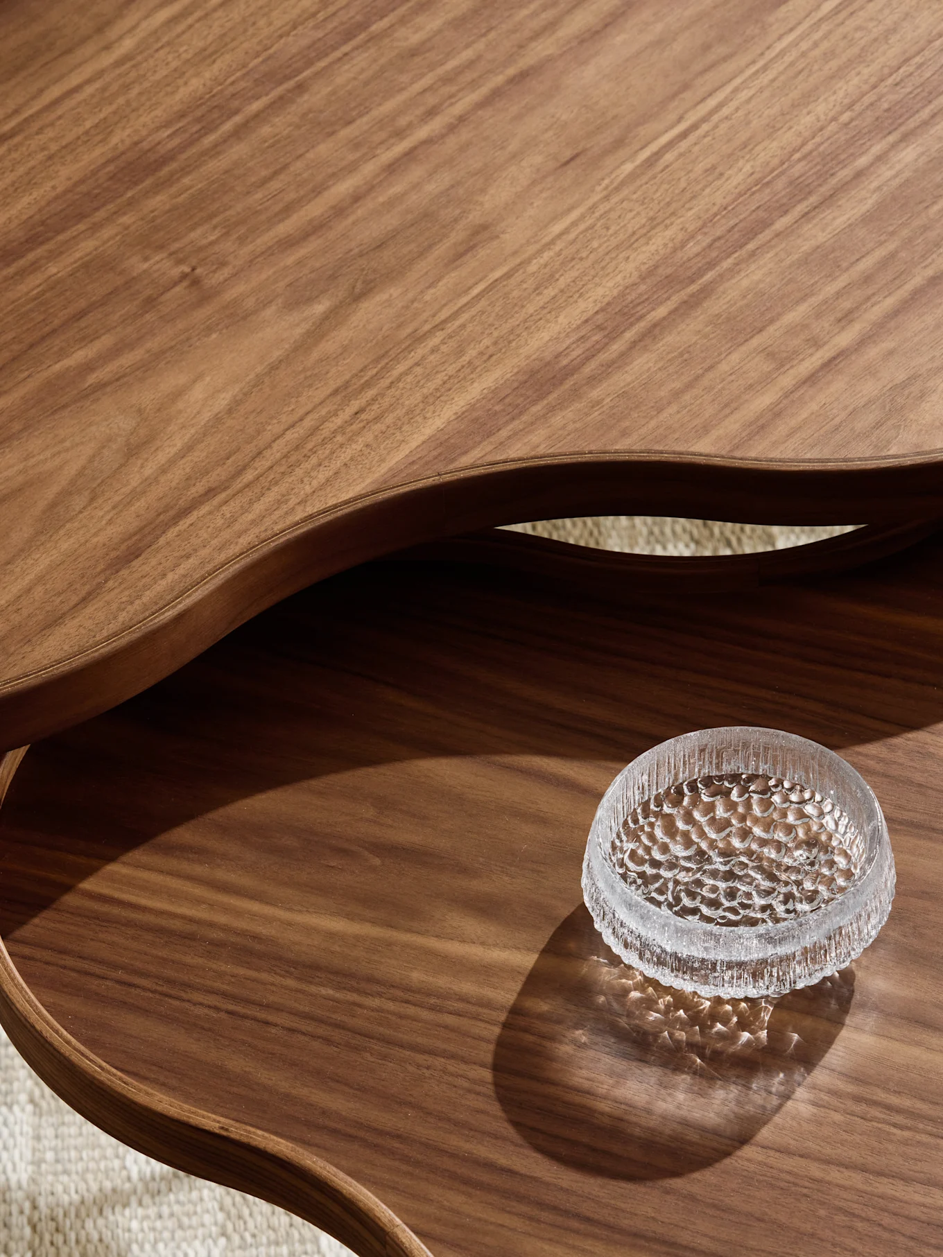 Close-up of a wavy two-tier wooden table with a textured glass coaster on the lower level.