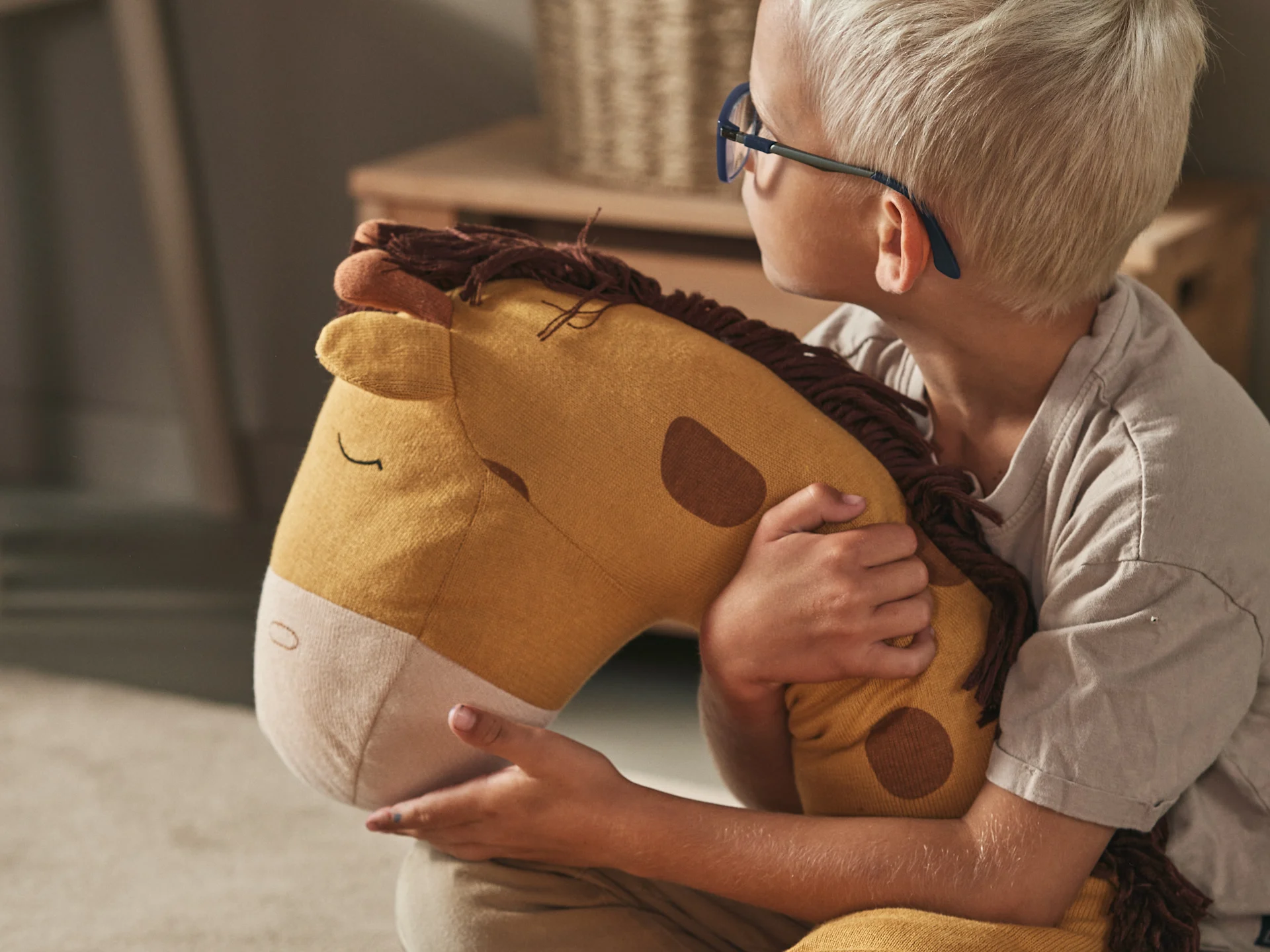 Young boy in glasses holding a mustard yellow stuffed horse with brown spots.