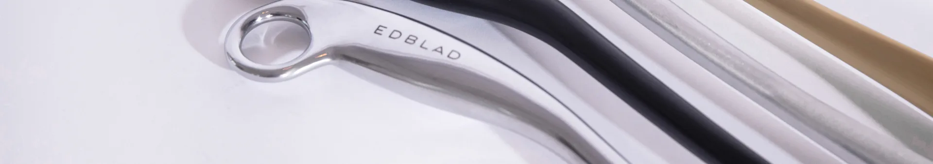 Close-up of a silver metallic object with "EDBLAD" engraved, alongside blurred black, white, and beige elements.