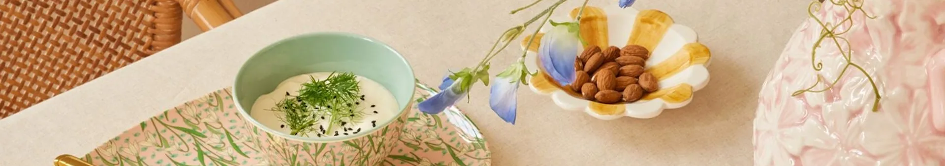 A mint bowl with dip, a scalloped bowl with almonds and a blue flower, and a pink vase on a table.