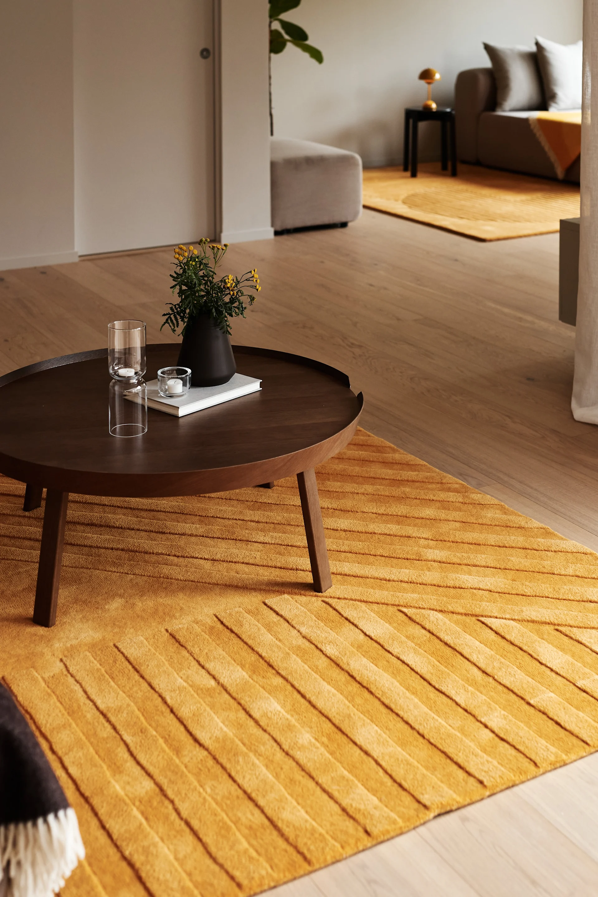 Warm living room with mustard yellow striped rug, dark wood coffee table, flowers, and candles.