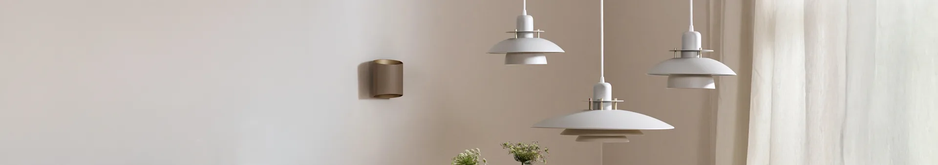 Three white multi-tiered pendant lights and a bronze cylindrical wall light on a light-colored wall with sheer curtains.