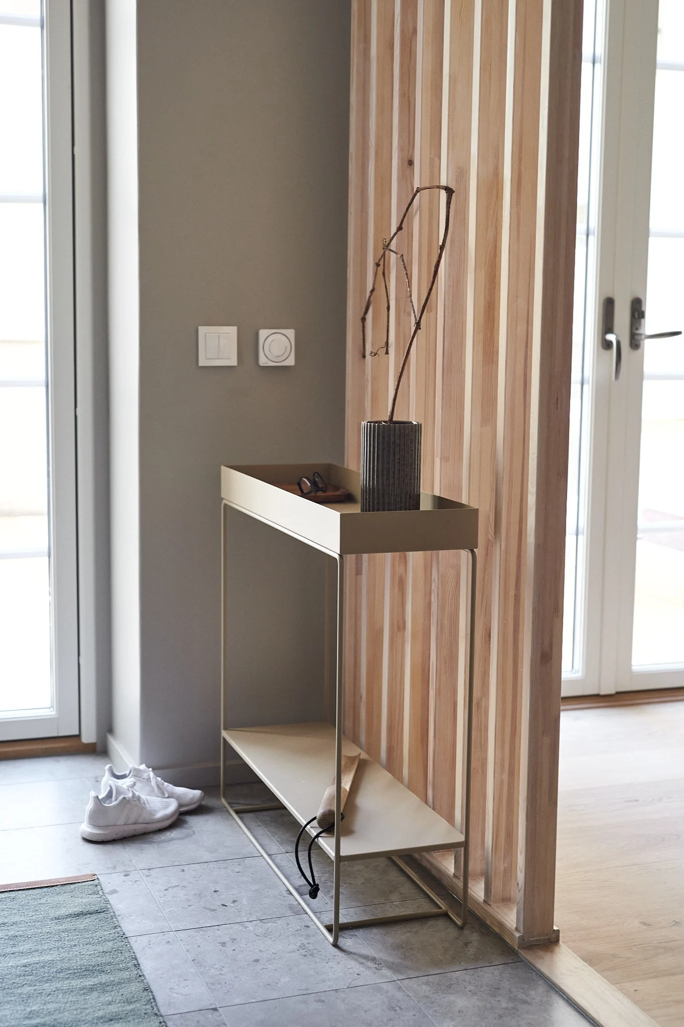 A minimalist entryway features a light metal console table with a vase and a pair of white sneakers on the floor.