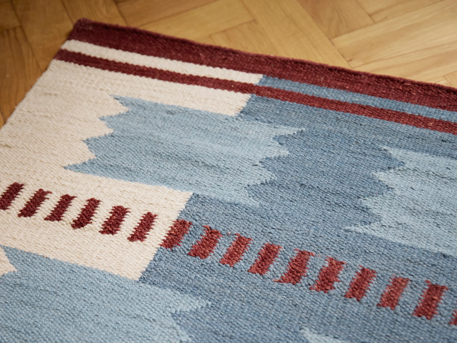 Woven rug with geometric patterns in blue, white, and burgundy on a wooden floor.