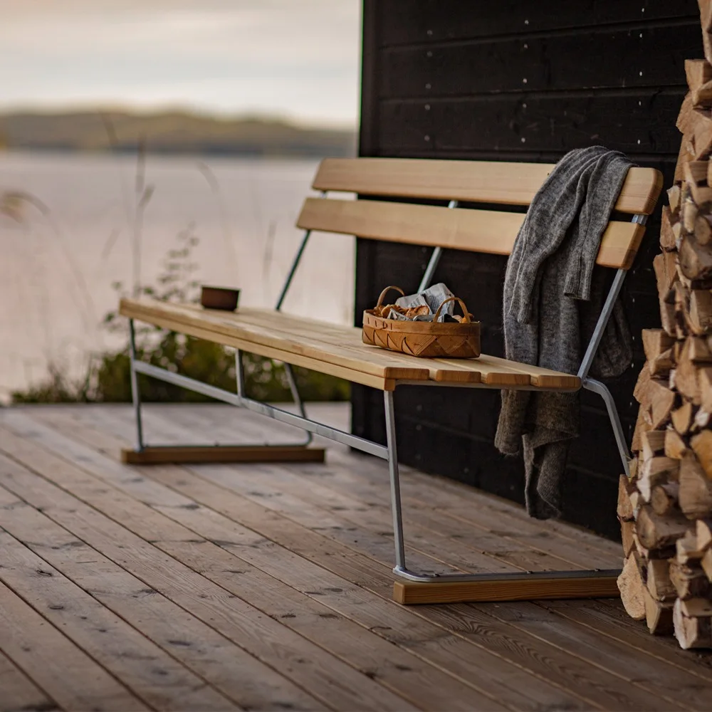 Wooden bench with a gray blanket, a woven basket, and firewood on a deck by a lake.