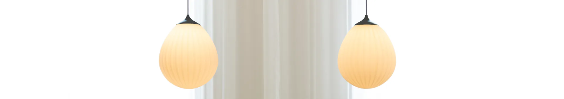 Two elongated, ribbed pendant lights with a warm glow hang against a light background.