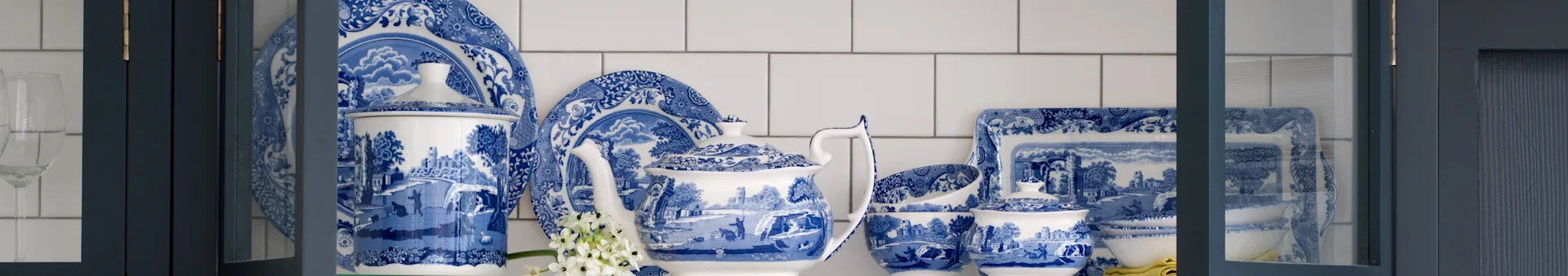 Blue and white patterned porcelain dinnerware set with a teapot, plates, and bowls in a dark blue cabinet.
