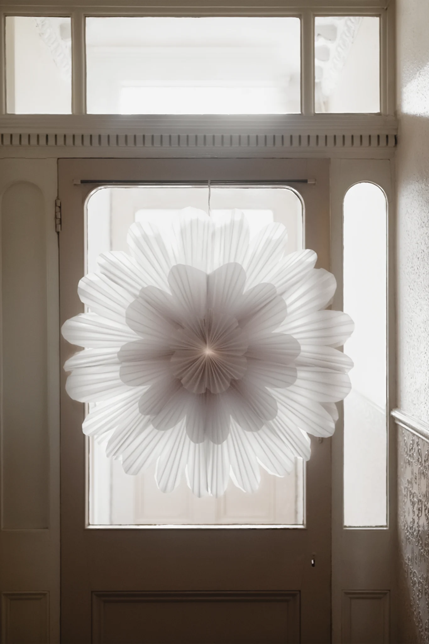 The snöblomma paper star from Watt & Veke hangs in a hallway on a front door with the light shining from behind. 