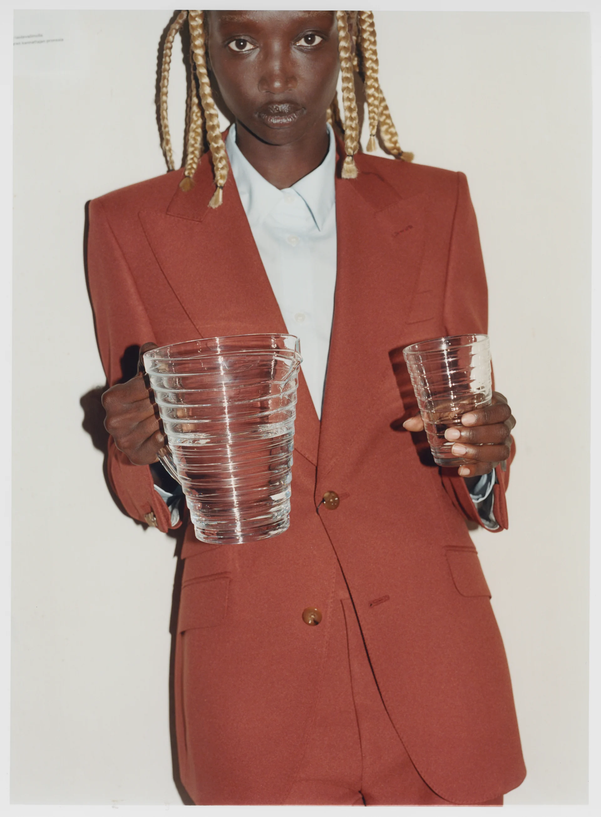 Person in terracotta suit holding a large glass pitcher and a small glass of water.