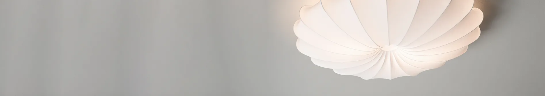 A white, sculptural ceiling lamp with radiating, pleated layers, illuminated from within against a light gray background.