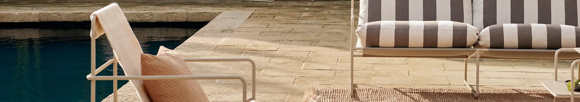 Two outdoor chairs with striped cushions on a stone patio beside a blue swimming pool.