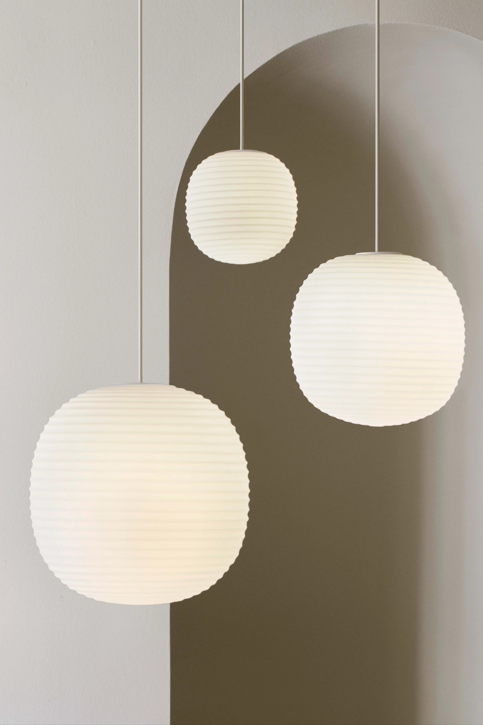 Three white, round, ribbed pendant lamps hang against a light gray wall with curved shadows.