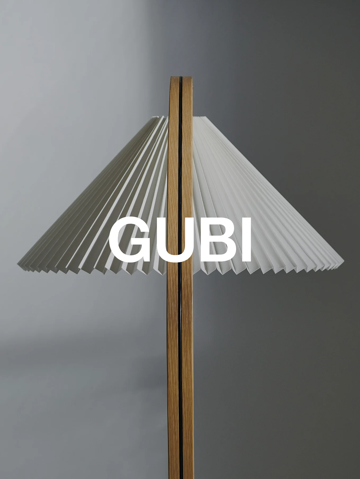 A lamp with a pleated white shade and a wooden stem, with 'GUBI' text overlay.