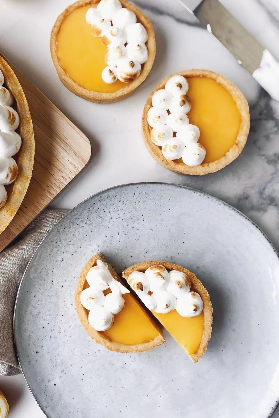 Lemon meringue tarts with toasted meringue peaks, one cut in half on a grey plate.