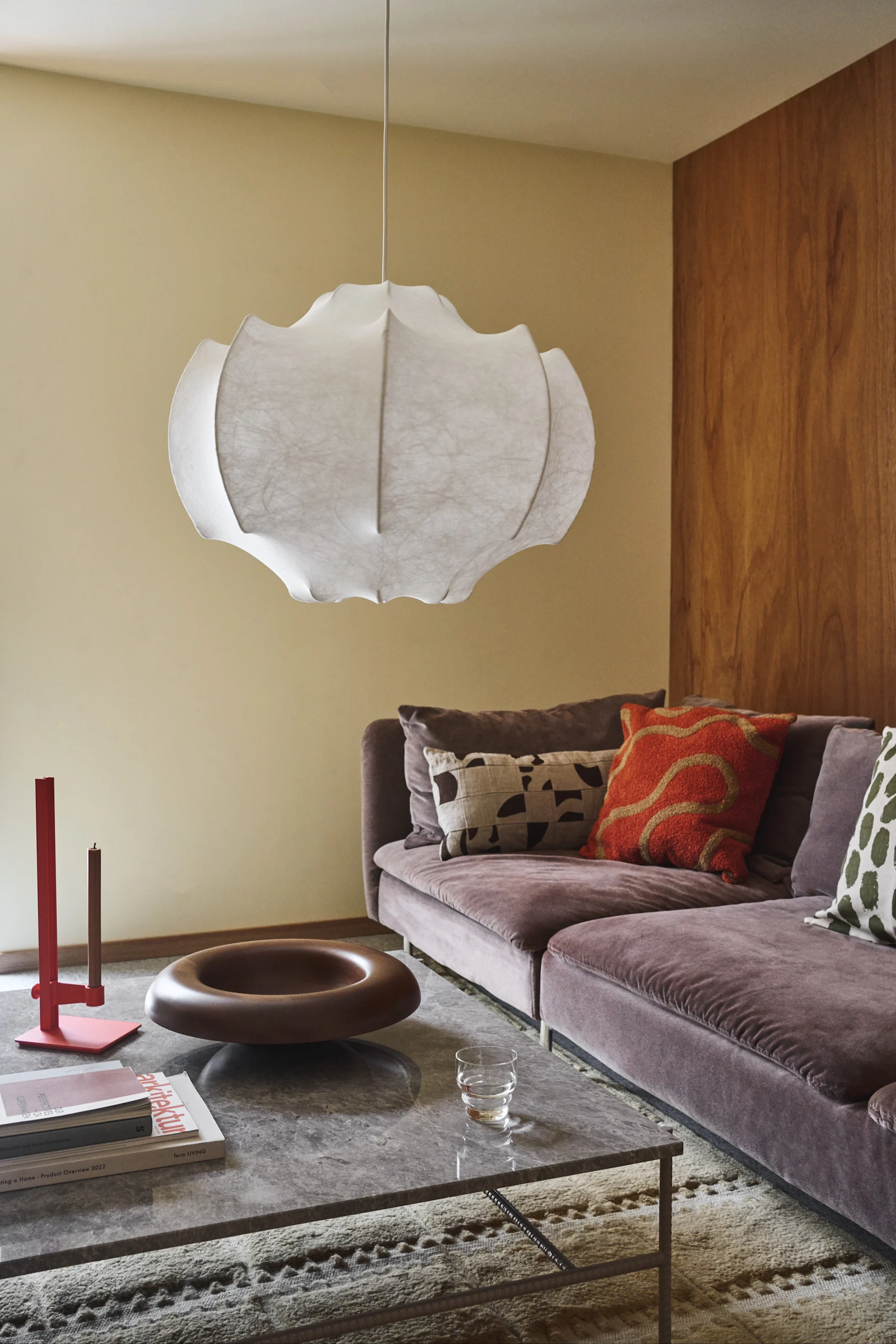 A modern living room with a large white pendant lamp, a purple velvet sofa with patterned cushions, and a marble coffee table.