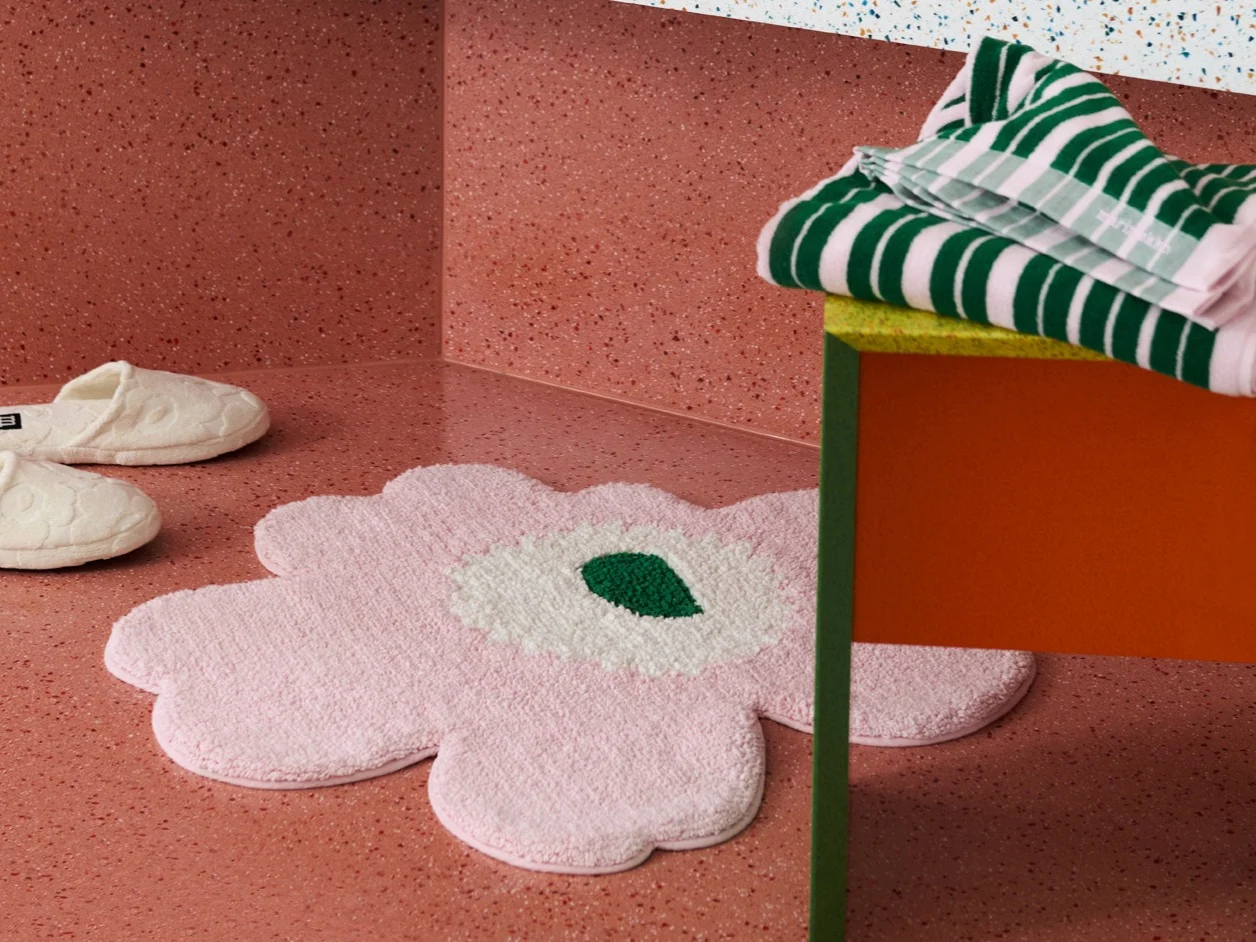 A pink flower-shaped rug, white slippers, and striped towels on a colorful table.