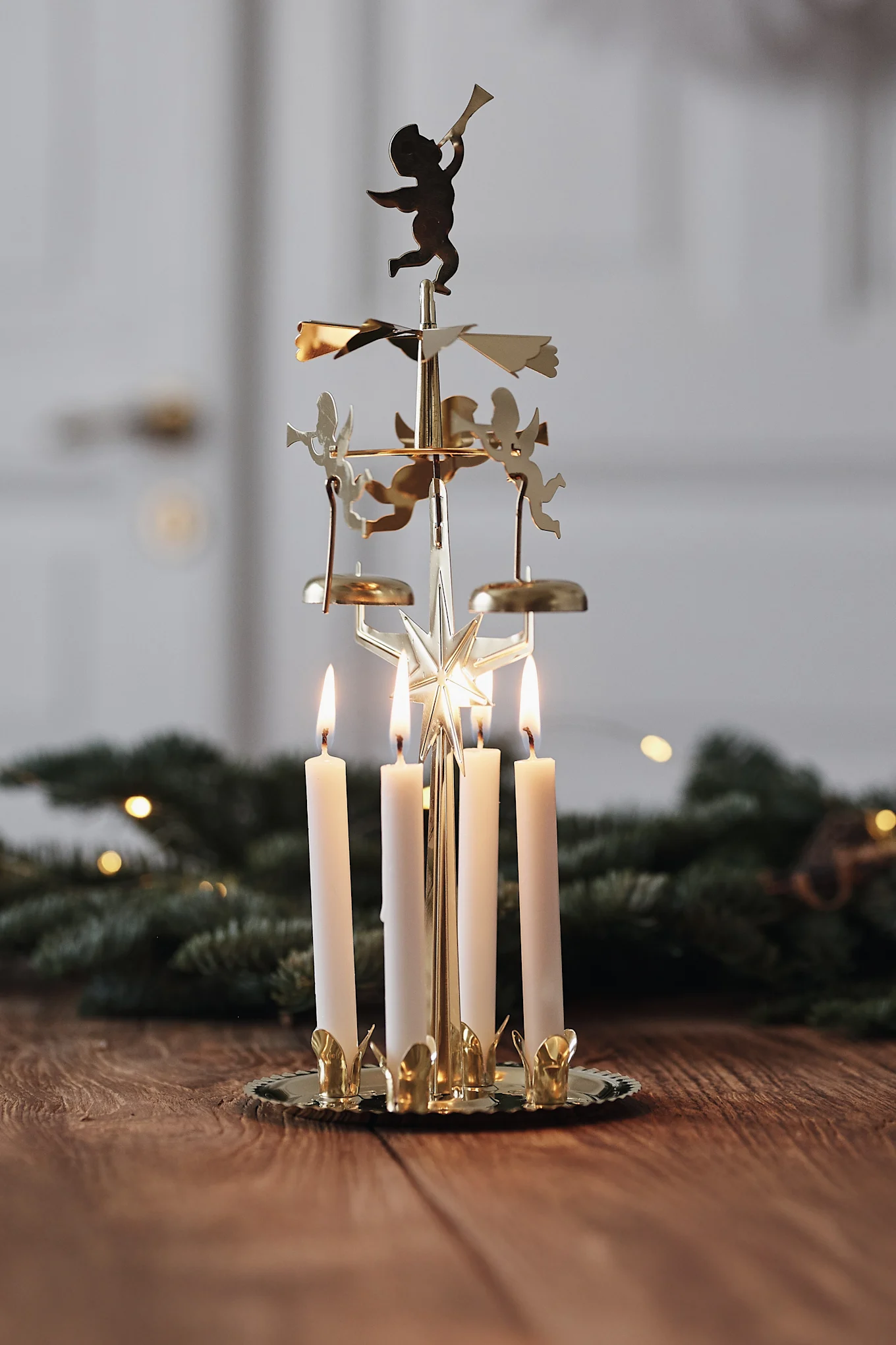 Golden Christmas carousel with four lit white candles and angel figurines on a wooden table.