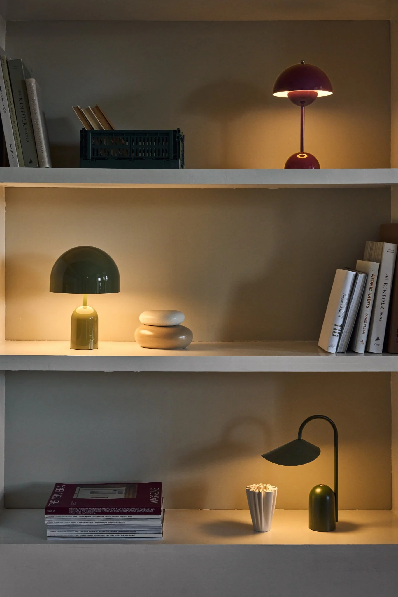 Three glowing green and burgundy table lamps on shelves with books and decor.