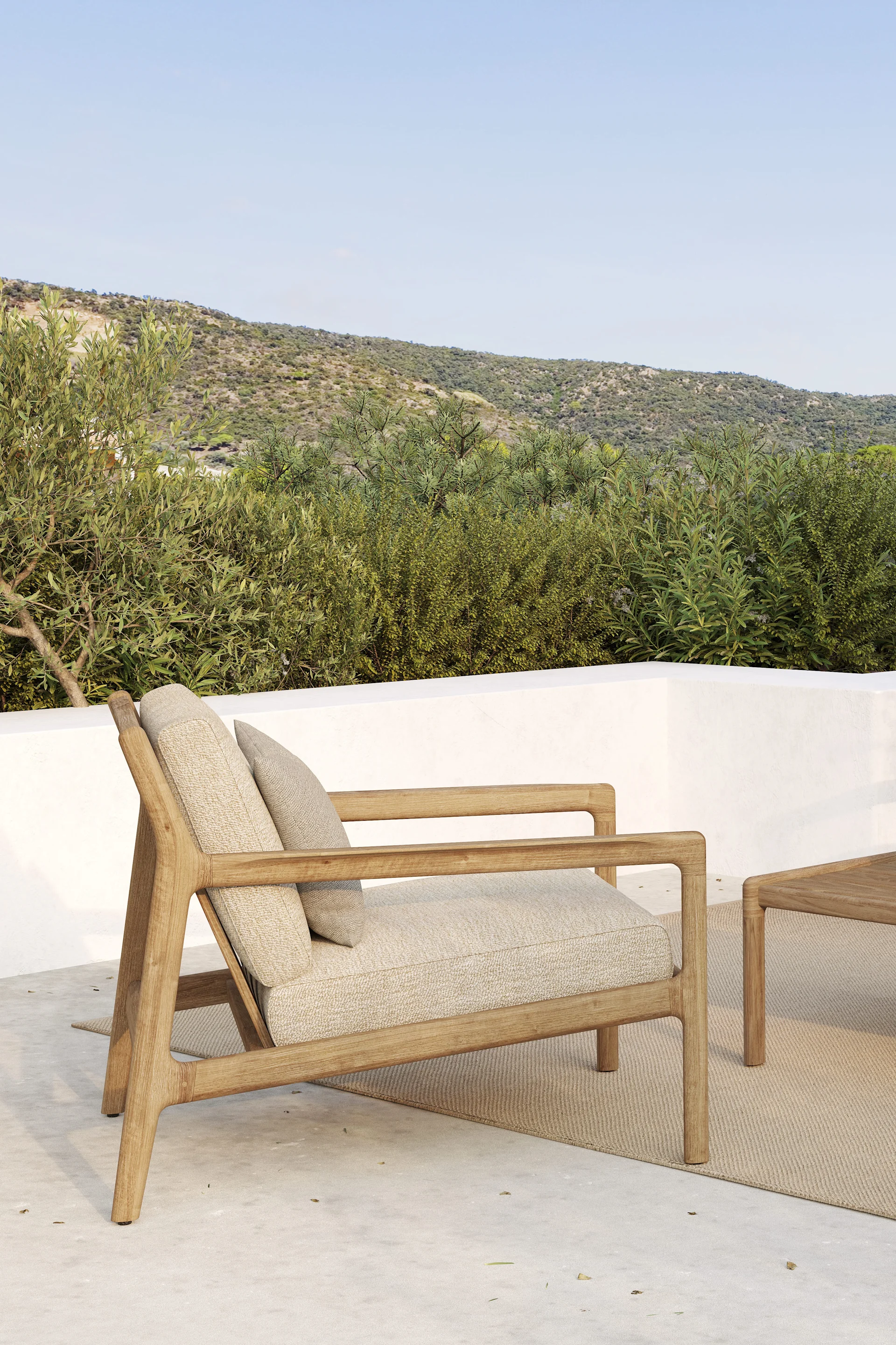 Wooden outdoor armchair with light cushions on a patio, set against green hills and a blue sky.
