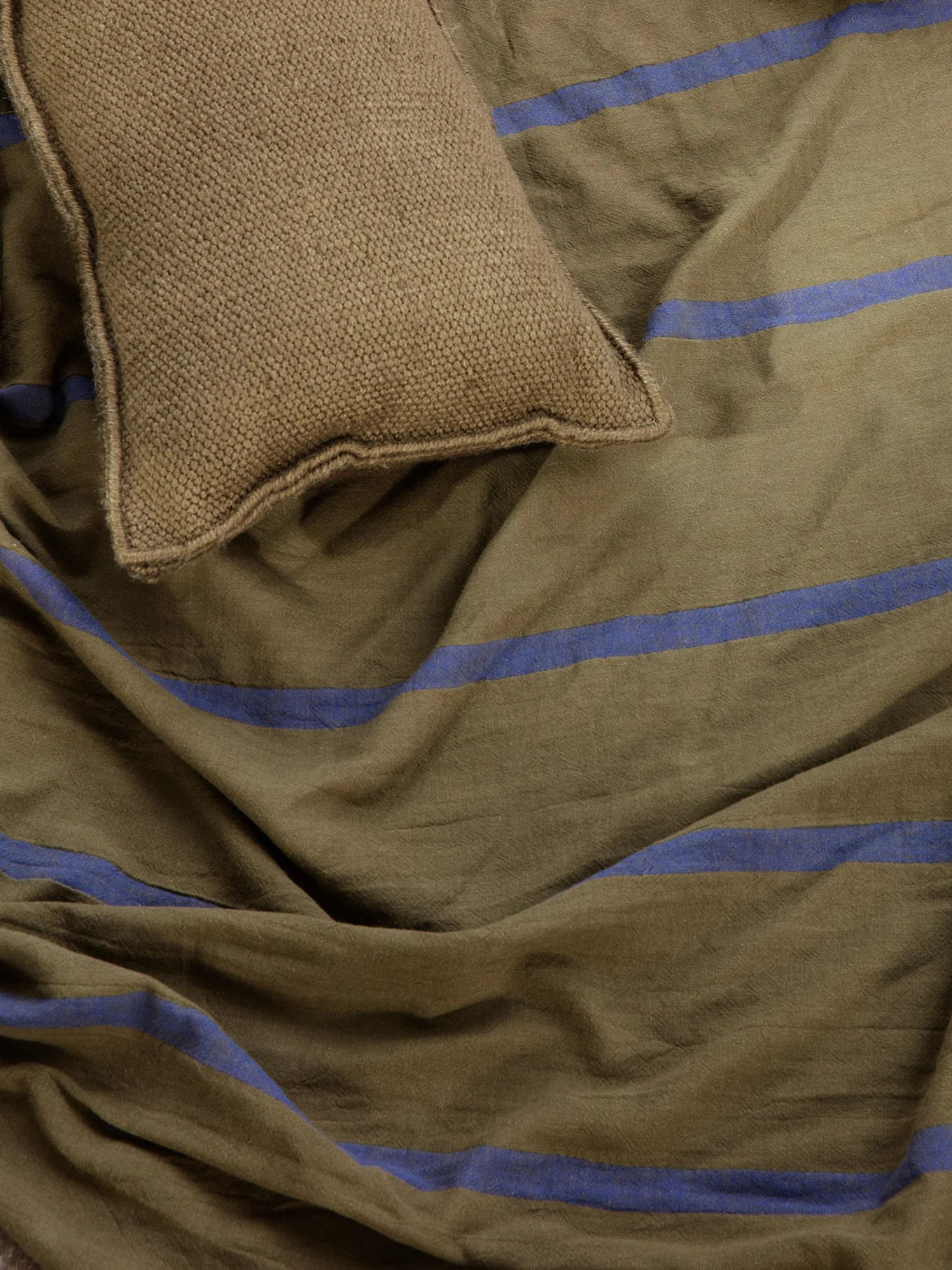 Brown knitted cushion on olive green striped fabric with blue stripes.