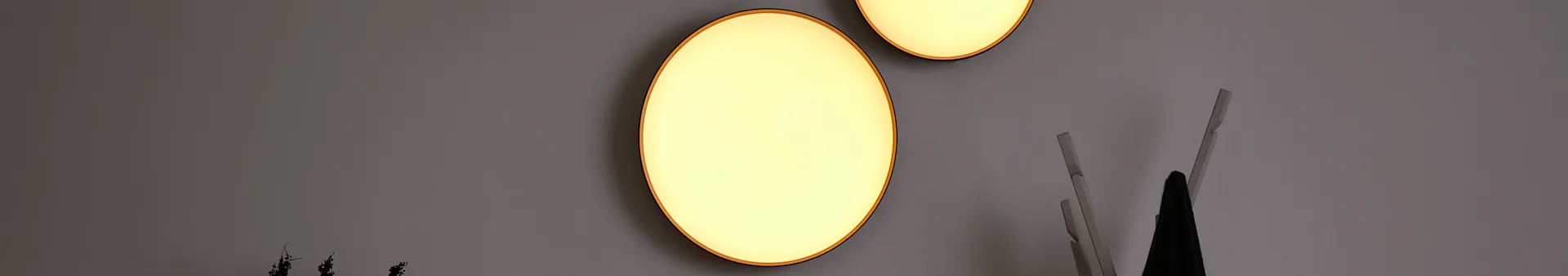 Two glowing oval wall lights against a grey wall, with a dark object and light wooden elements in the foreground.