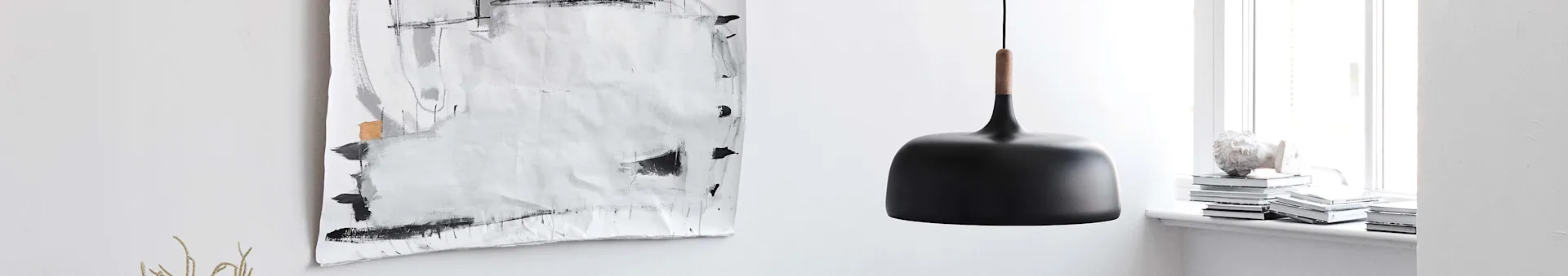 Black modern pendant lamp with a wooden detail, next to abstract art and books on a windowsill.