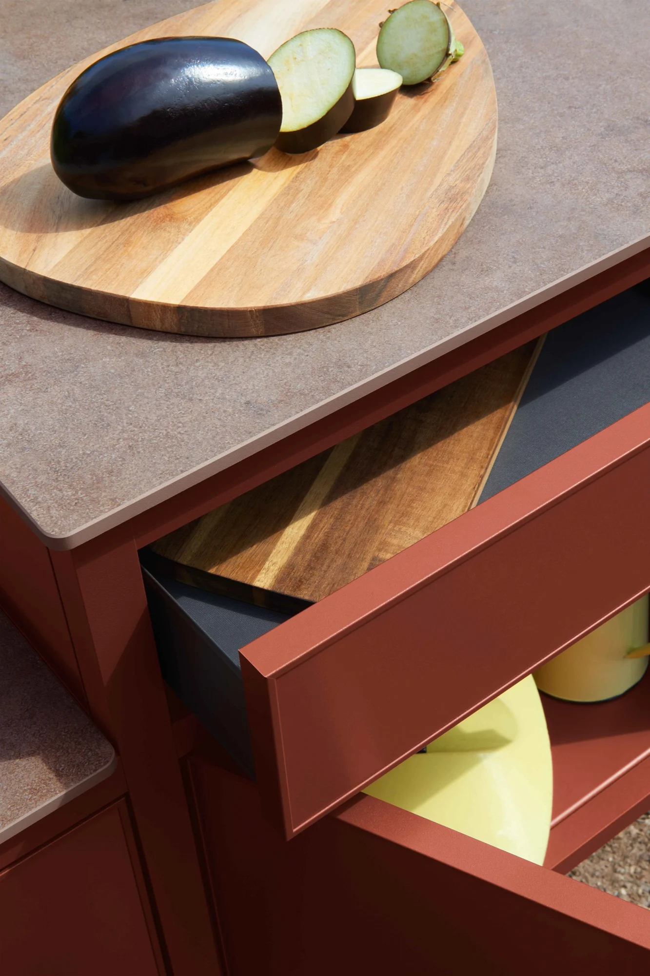 Whole and sliced eggplant on a wooden cutting board on a speckled countertop, with an open reddish-brown cabinet drawer below.