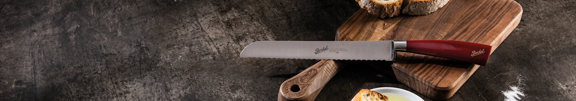 Serrated bread knife with red handle on a wooden board with sliced bread.