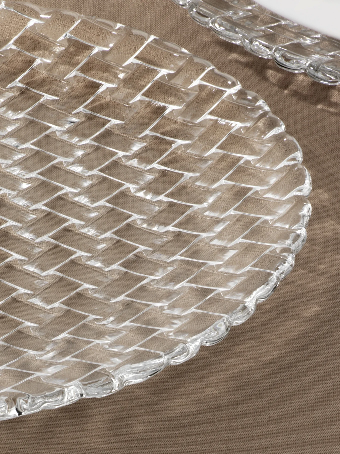 Clear glass plate with a woven basketweave pattern on a brown fabric surface.
