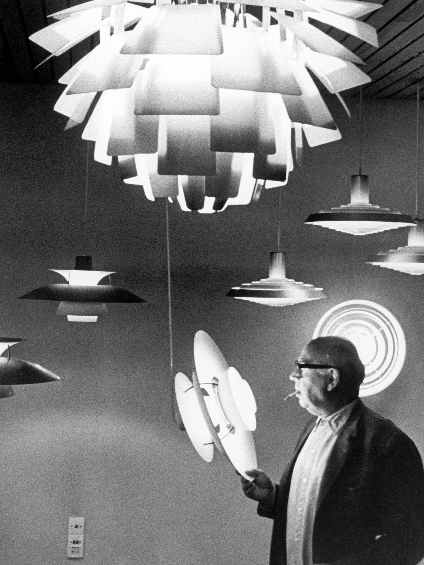 Man with glasses and cigarette inspecting several layered, modern lamps in black and white.