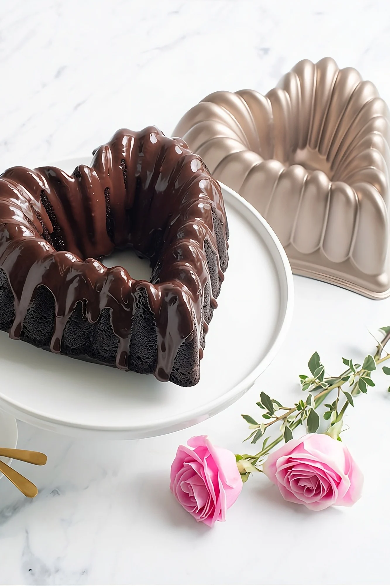 Heart-shaped chocolate cake with ganache, heart-shaped bundt pan, and two pink roses on marble.