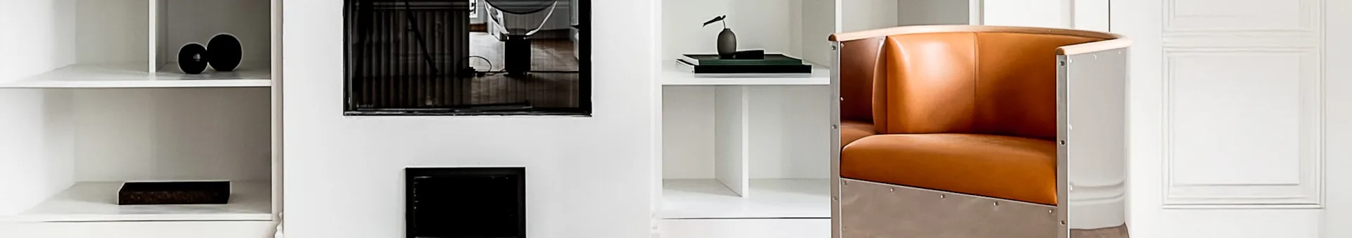 A white shelving system with decorative items and a brown leather armchair with metal rivets.