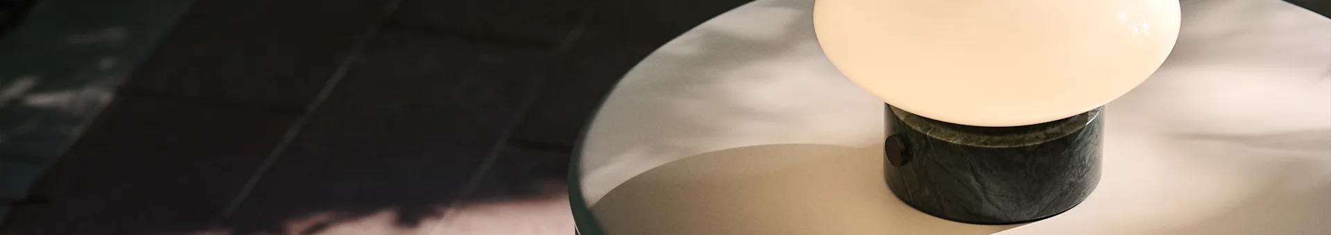A modern table lamp with a spherical light, a dark green marble base, casting a soft glow on a light surface.