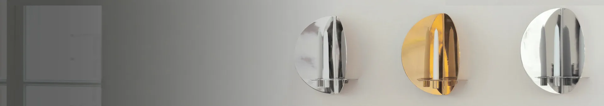 Three metallic oval wall sconces, two silver and one gold, each holding two white candles.