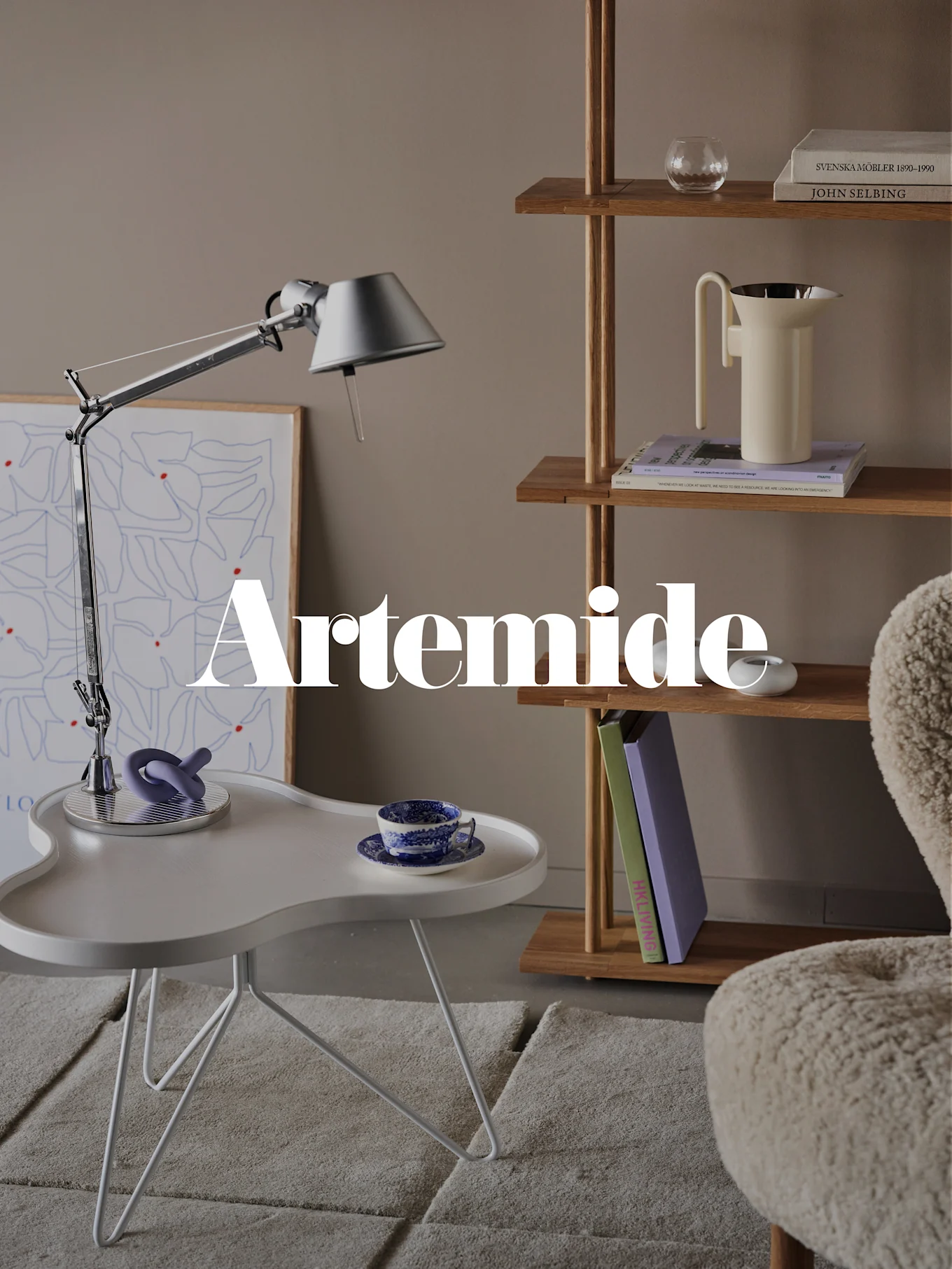 A modern living room with a silver desk lamp, white side table, wooden bookshelf, and a cream armchair. Text overlay: 'Artemide'.