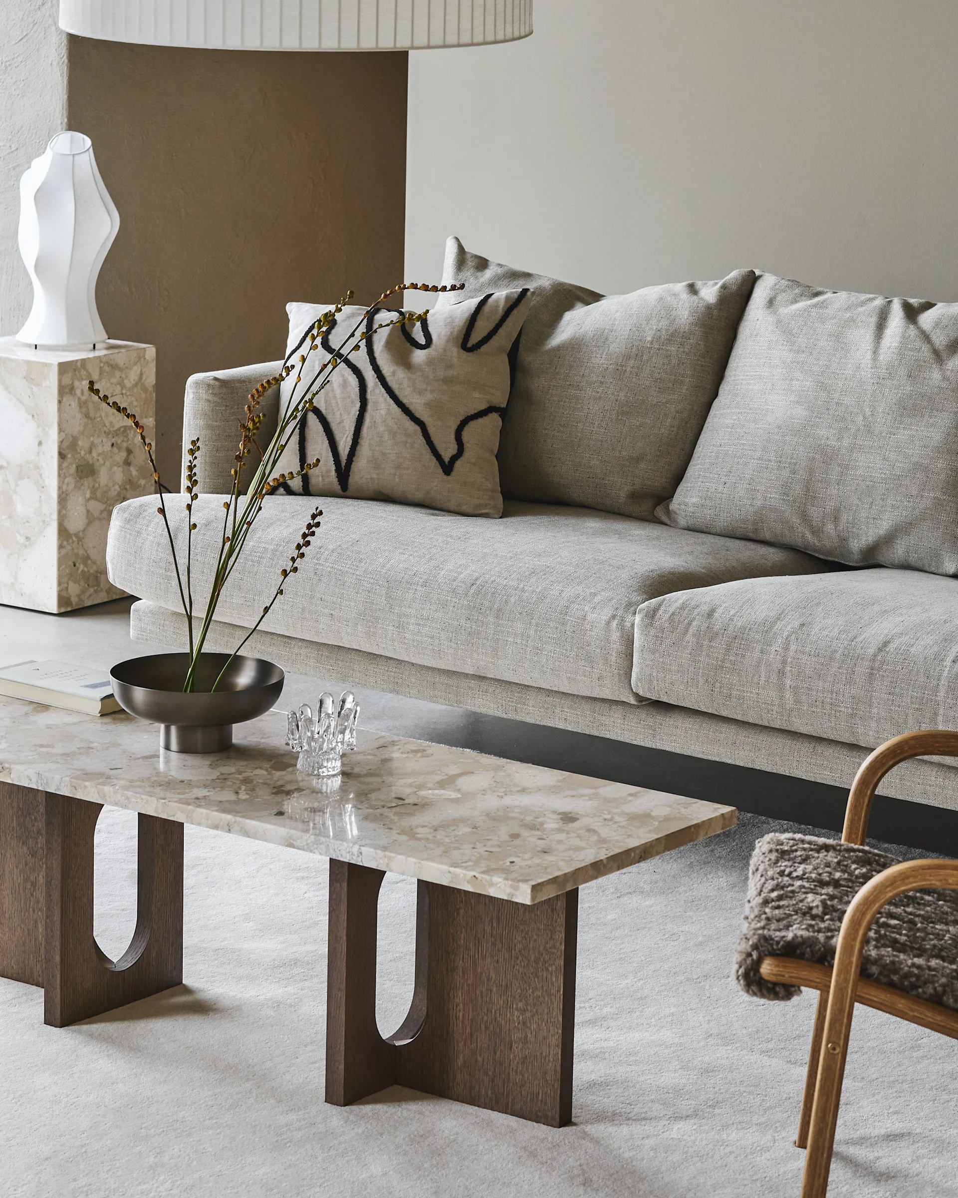 A modern living room with a light grey linen sofa, a marble coffee table, a patterned cushion, and a sculptural white vase.