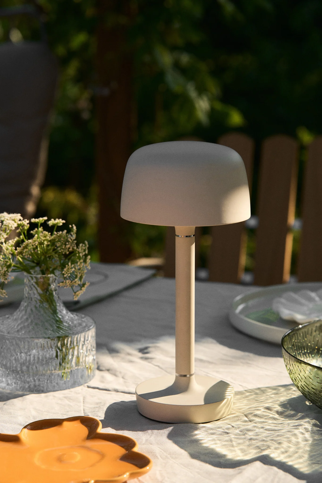 A mushroom-shaped beige table lamp on a white outdoor dining table with flowers and dishes.