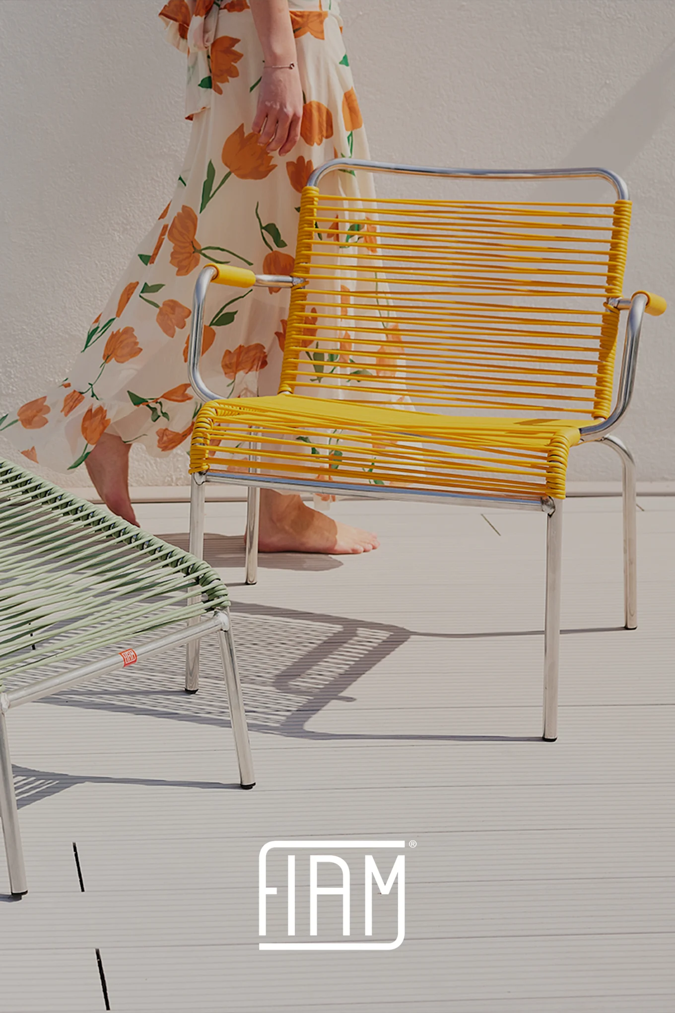 Person in floral dress next to yellow and green woven string outdoor chairs.