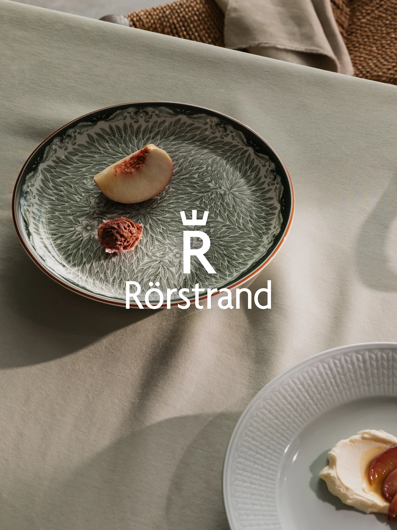 Rörstrand plates on green linen: one dark green patterned with peach, another light grey with cream and fruit.