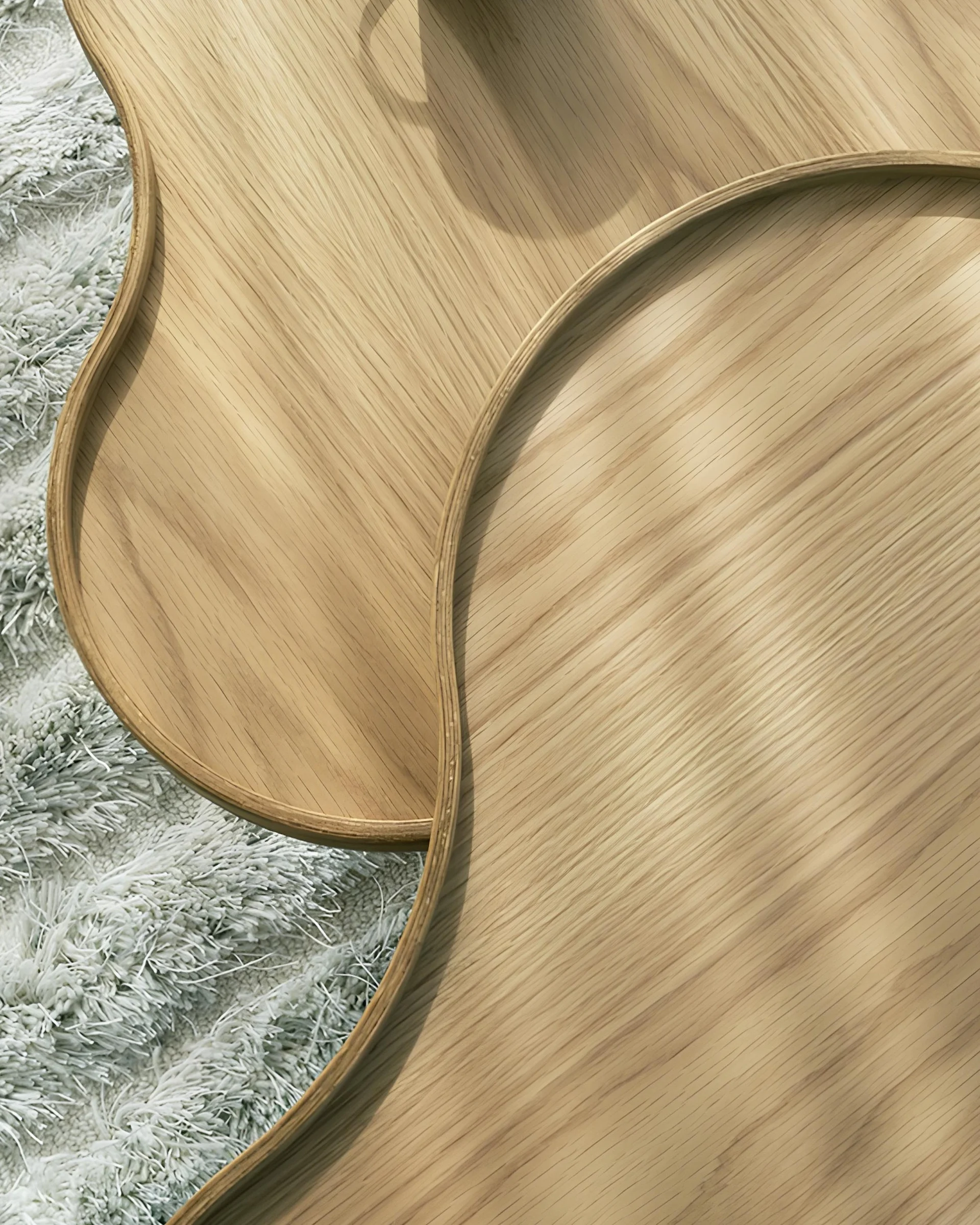 Two curved light wood trays overlapping on a fluffy white rug, with a cup's shadow on the top tray.