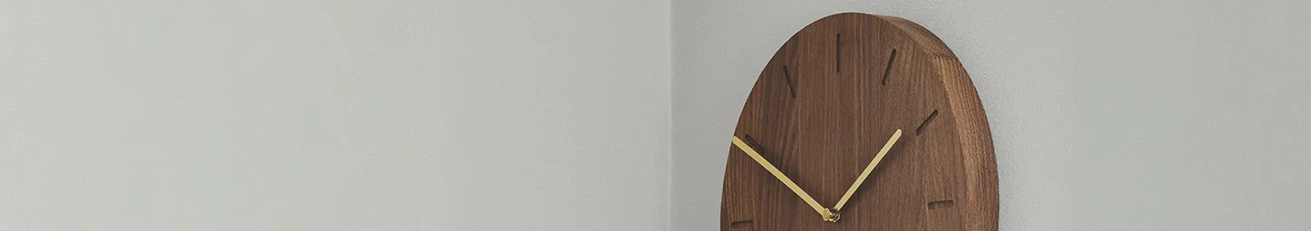 Minimalist wooden wall clock with gold hands on a light gray wall.