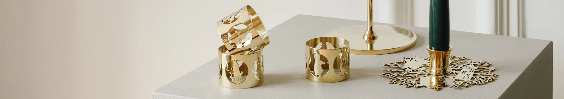 Gold Moomin-patterned candle holders next to a green candle with a decorative gold snowflake base.