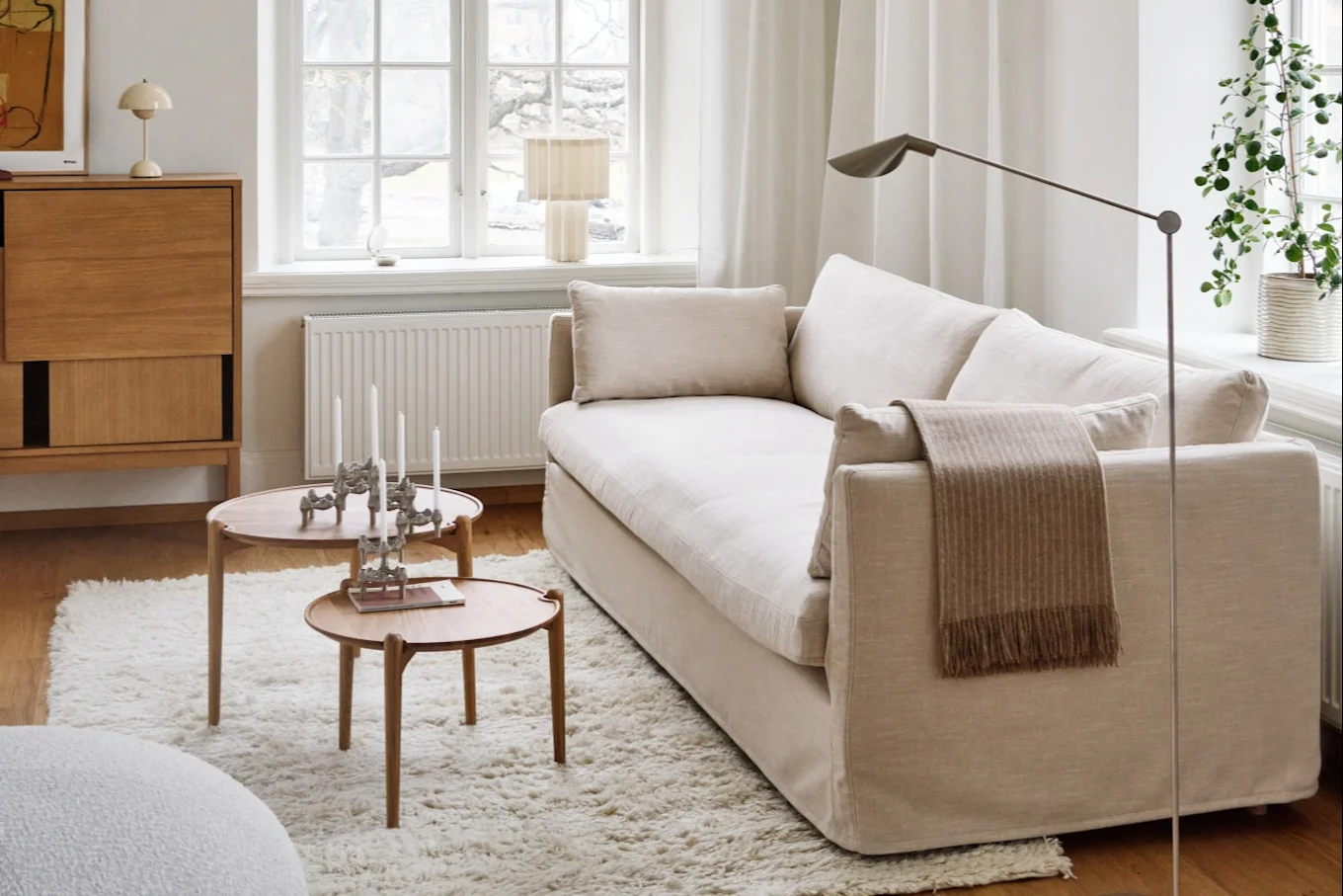 A cozy living room with a light-colored sofa, two round wooden coffee tables, a shaggy rug, and a wooden cabinet.