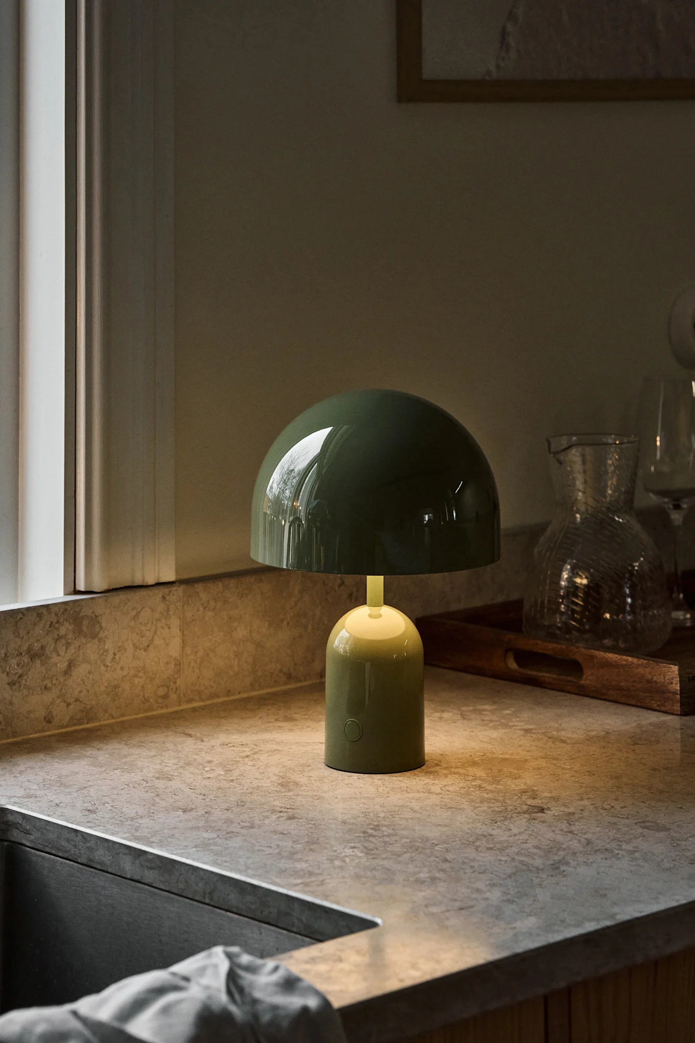 A dark green mushroom-shaped table lamp with a soft glow sits on a mottled countertop next to a window.