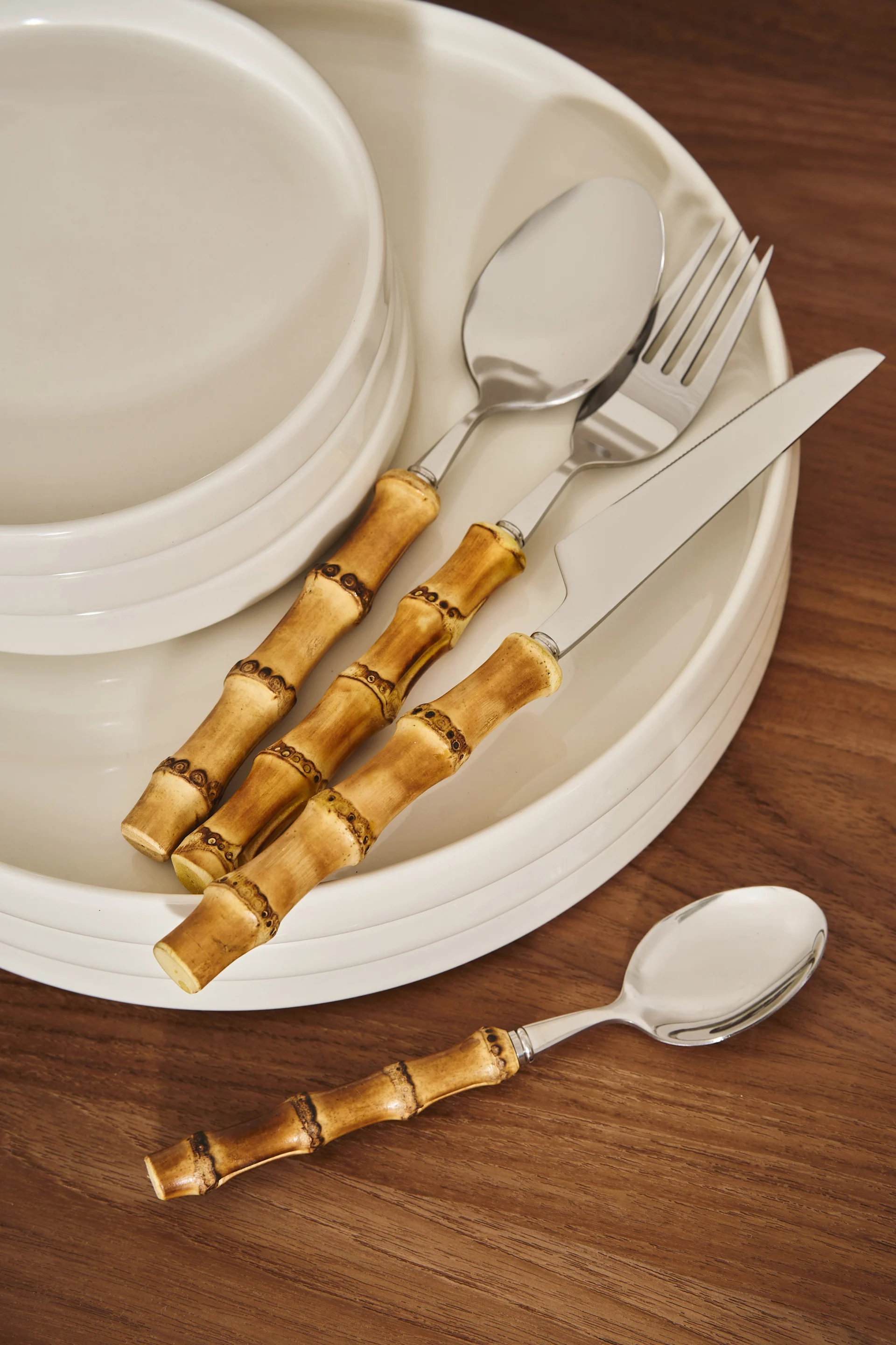 Bamboo-handled cutlery set (knife, fork, spoons) resting on white plates and a wooden table.