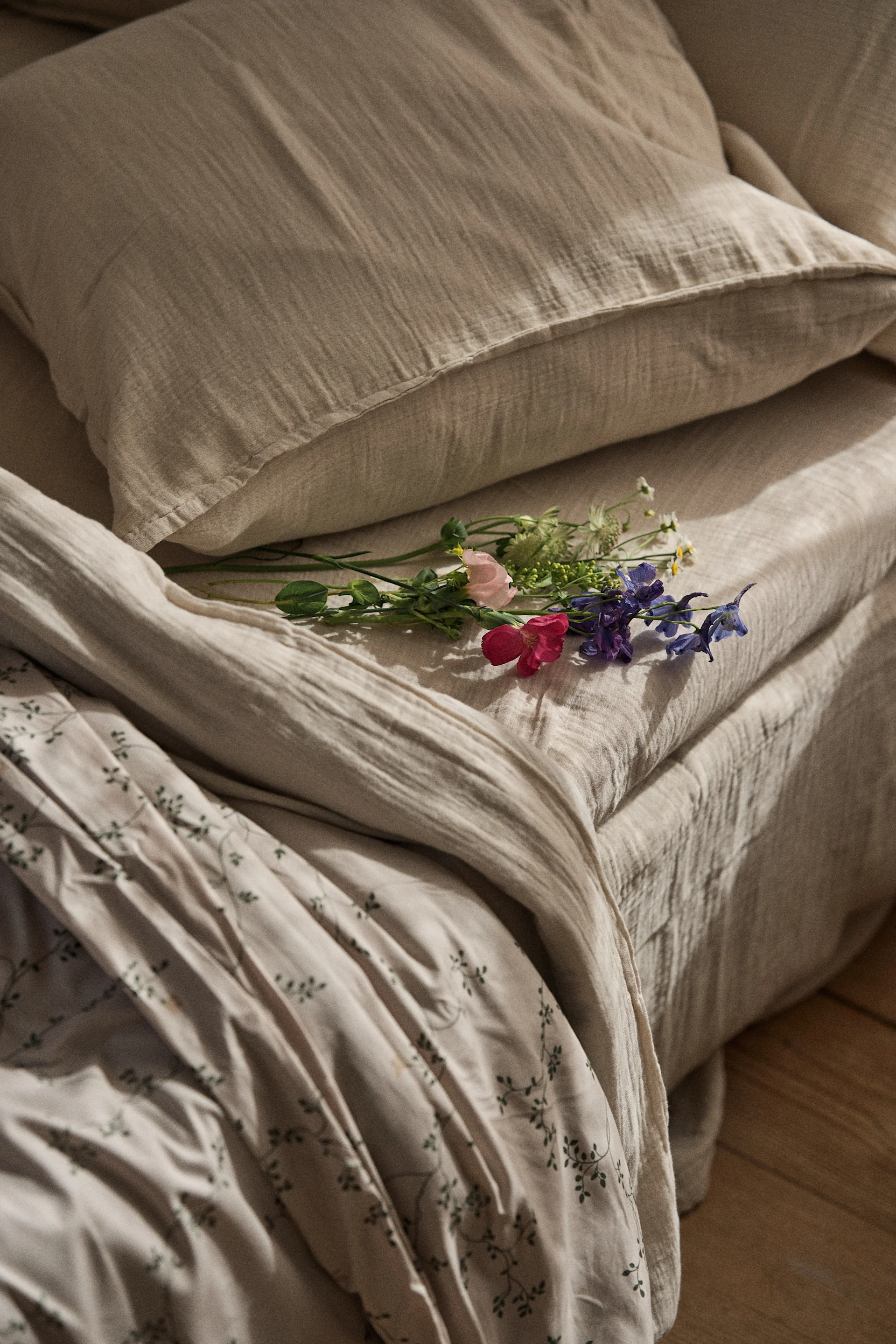 Colorful wildflowers resting on neutral-toned linen bedding with a subtle green leaf pattern on the duvet.