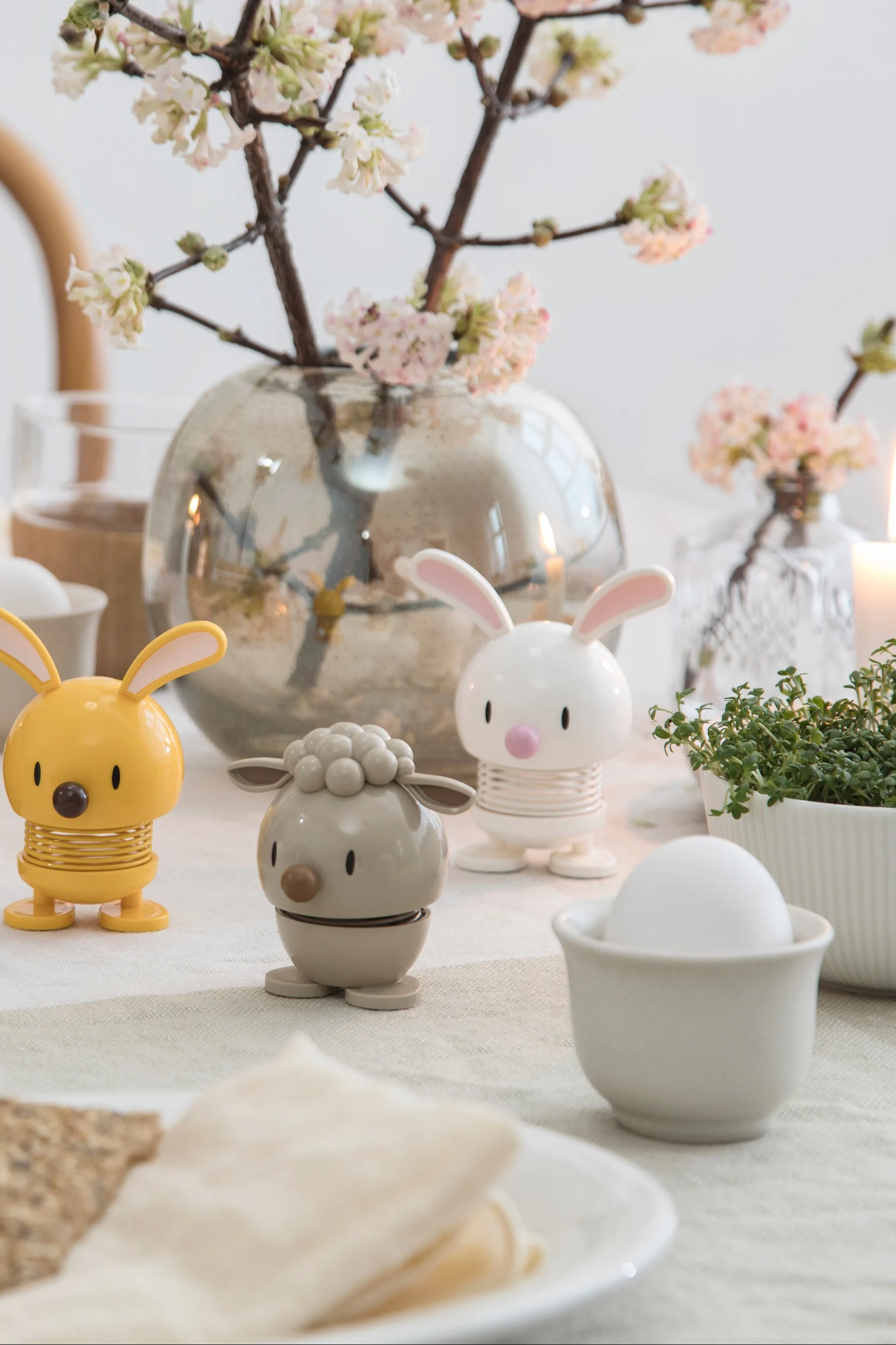 A spring table setting with animal-shaped egg holders, fresh flowers, and a lit candle.