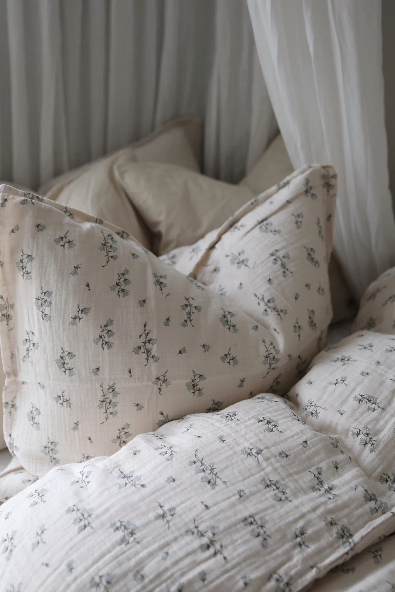 Cozy bedding set with light beige crinkled fabric and a delicate blue floral pattern, with soft white curtains.